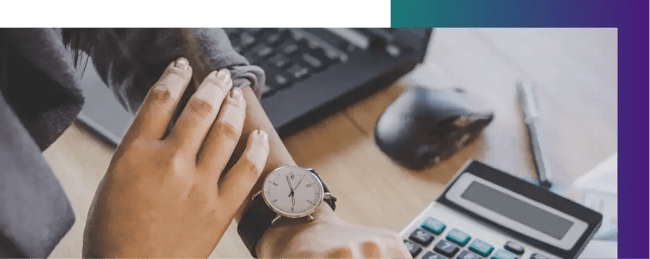 A woman checking the time on their watch as the manually calculate their financial accounts.