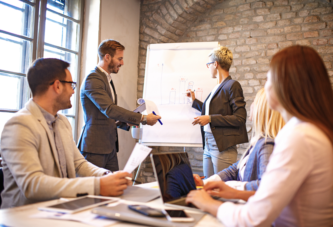 Business team in a meeting discussing financial data with charts on a flipboard presentation.