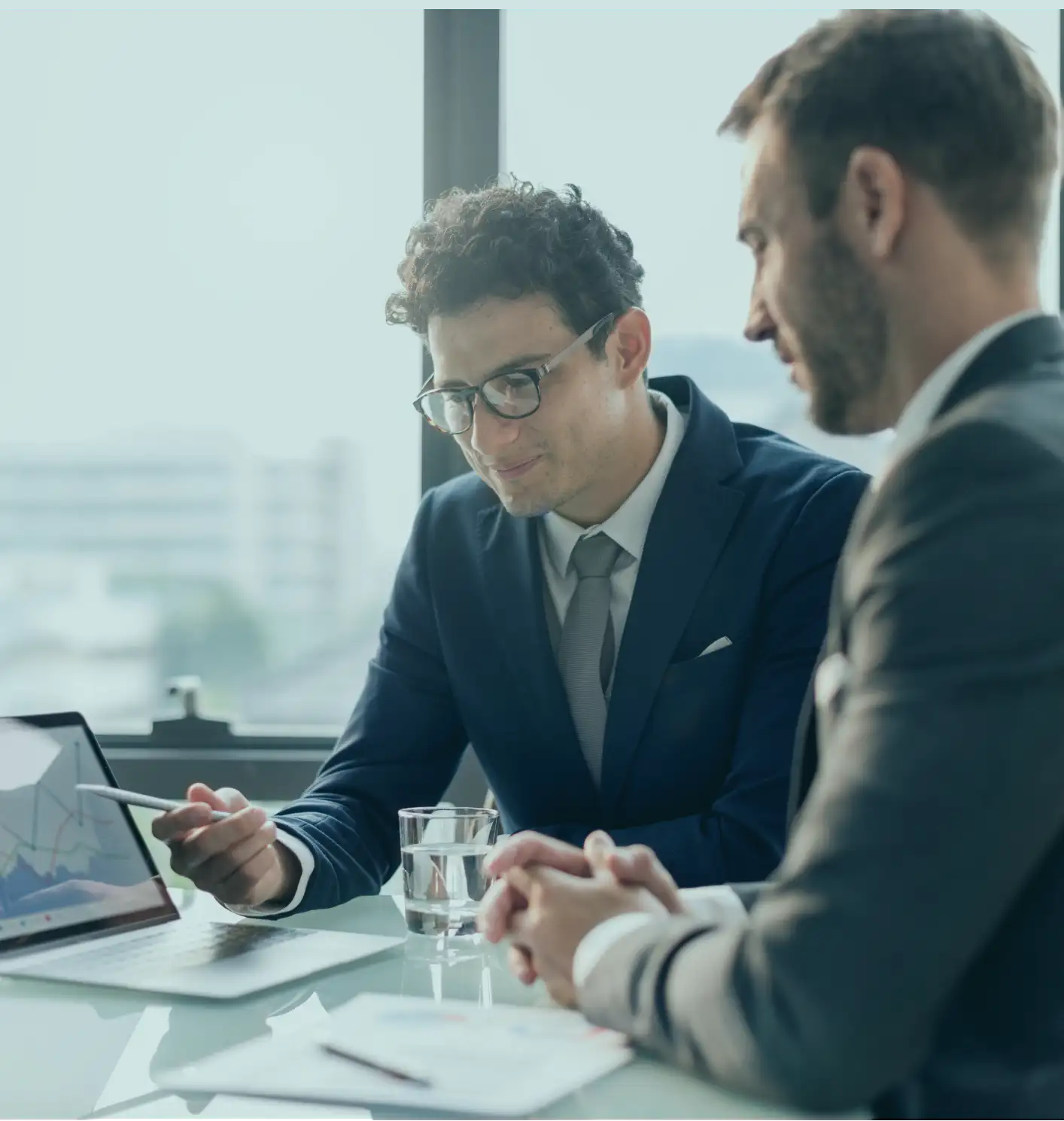 Two office workers looking through financial data on a laptop.