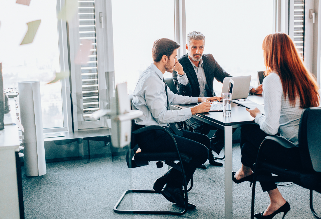 Business professionals in a meeting discussing financial strategies with laptops in a modern office setting.